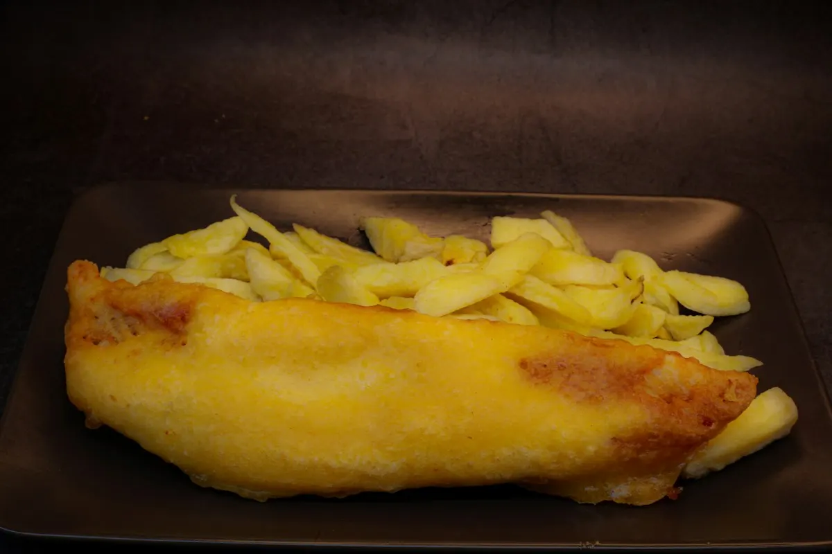 A long piece of battered fish with chips on a dark plate