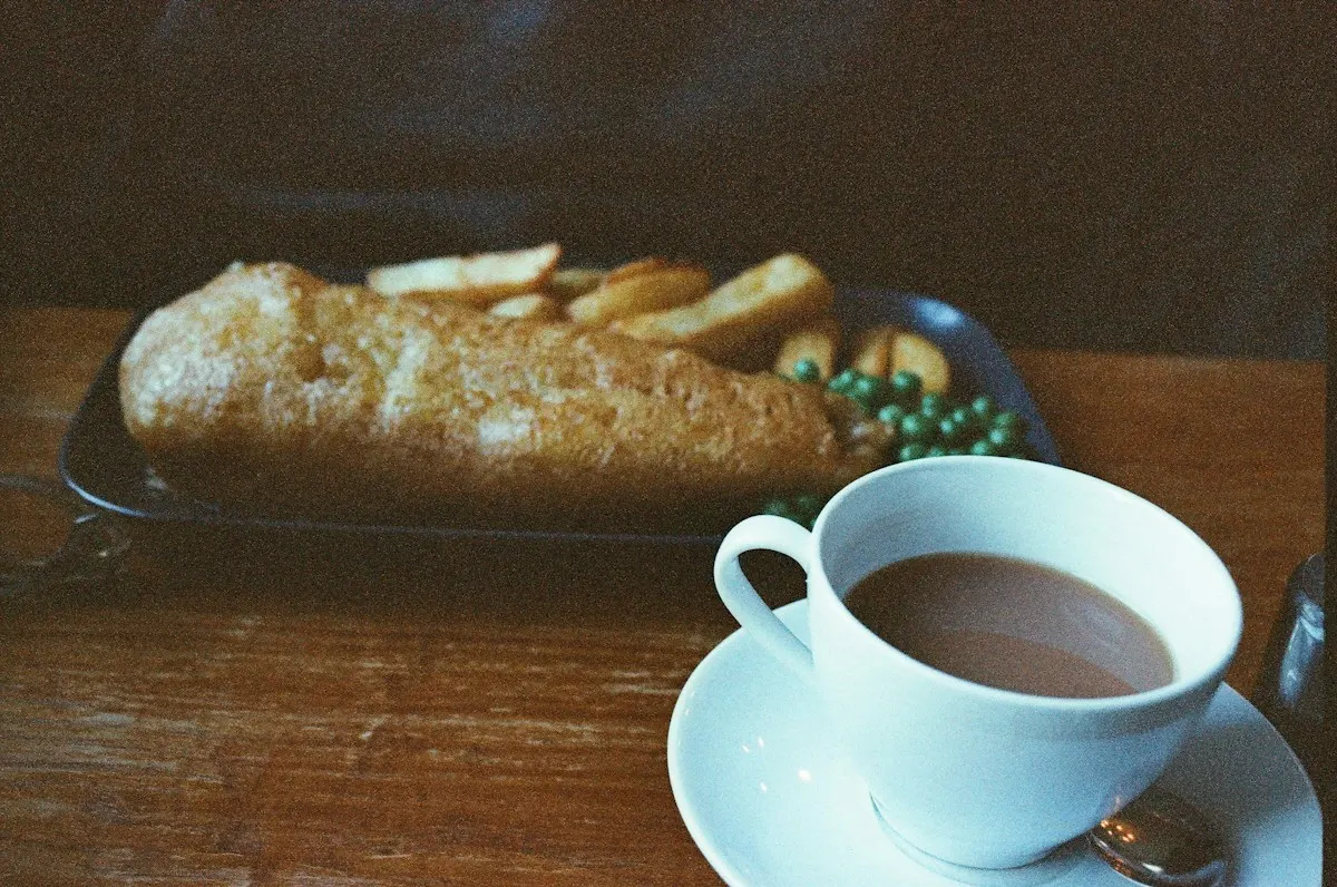 Fish and chips with peas next to a cup of tea