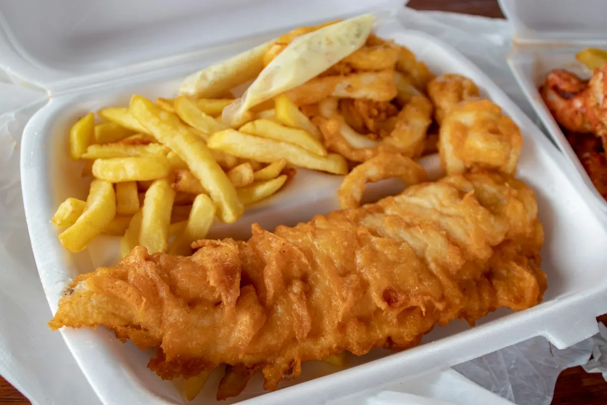Battered fish and chips with a lemon wedge in a takeaway tray